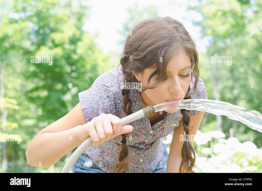 woman drinking water from garden hose E7PF9J